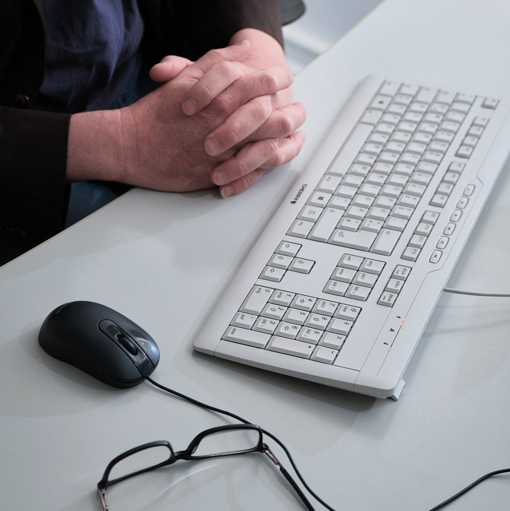 Gefaltete Hände neben einer Tastatur und einer Maus